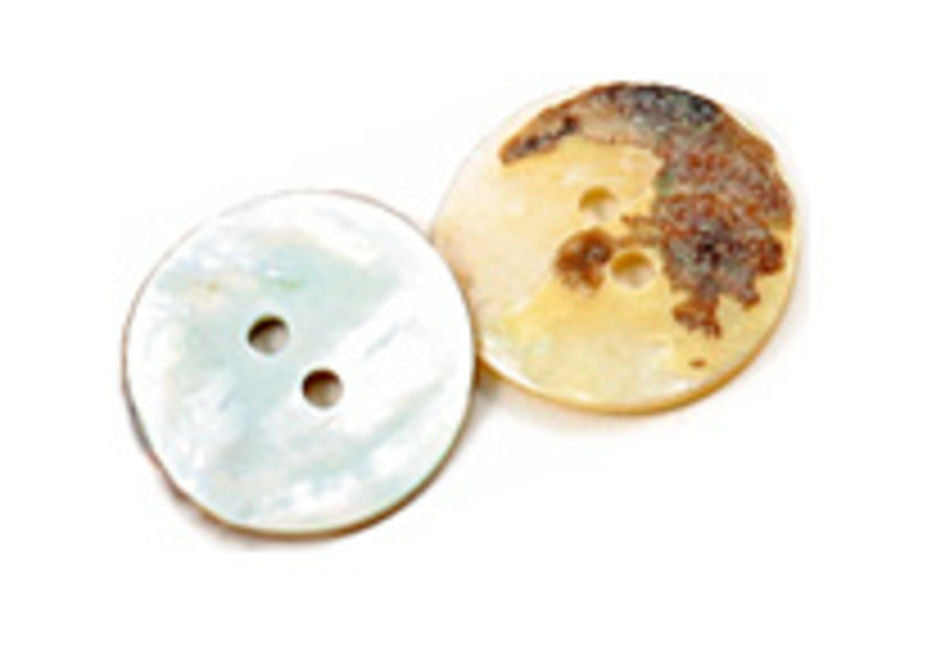 Two circular buttons, each featuring two holes, are positioned side by side on a white background. The button on the left, identified as a Natural Pearl Shell Button from Dill Buttons of America, Inc., showcases a pearly white and smooth finish reminiscent of Mother-Of-Pearl. In stark contrast, the button on the right appears discolored and worn with a brownish patch.