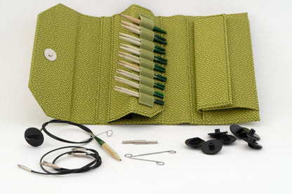 The Lykke 3.5" Interchangeable Bamboo Knitting Needle Set by Knitting Fever / Euro Yarns features a green textured fabric case with multiple bamboo knitting needles of various sizes, organized in neat rows. This beautiful collection includes knitting accessories such as cables, cable connectors, tightening keys, and end caps, all spread out in front of the case.