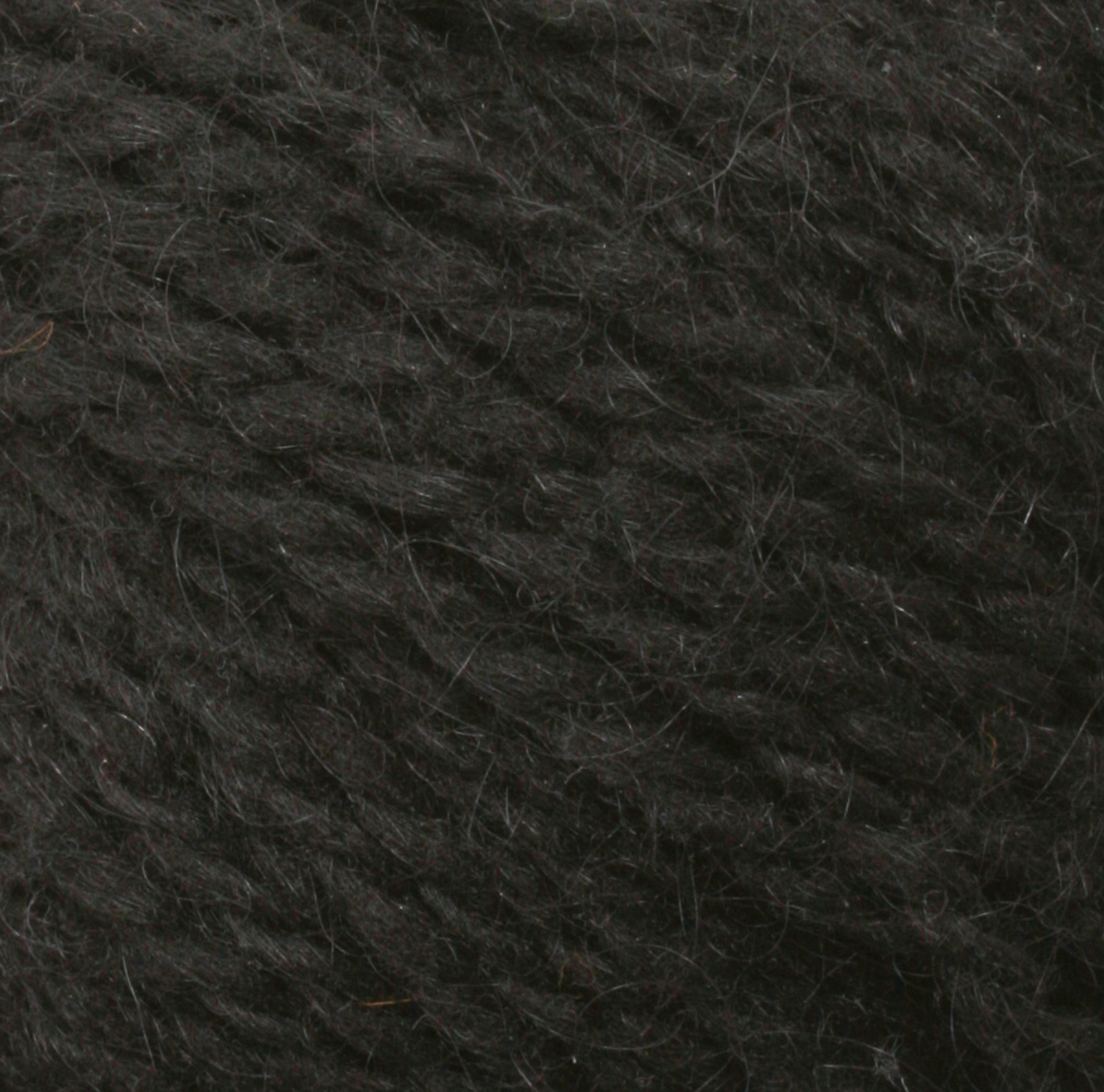 A close-up image of a textured, dark grey Harrisville Designs Peace Fleece Yarn. The fibers appear soft and slightly fuzzy, with a subtle shine from the natural wool and mohair blend. The yarn strands are densely intertwined, indicating it is tightly spun, making it perfect for worsted weight knitting projects.