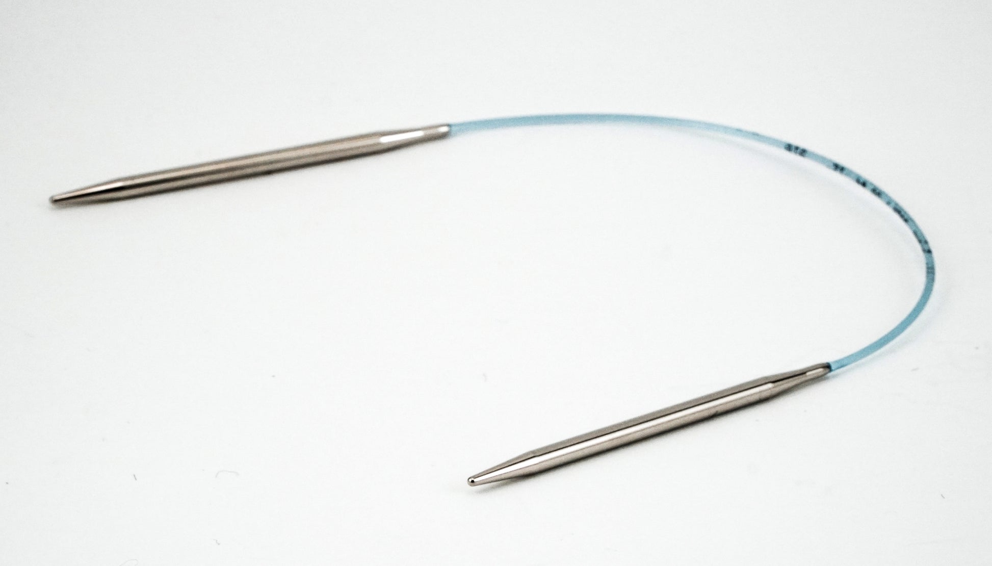 A pair of Addi Turbo Circular Knitting Needles by Skacel, characterized by metal tips connected by a flexible blue plastic cable, displayed on a solid white background. The needles are arranged in an arch shape, making them perfect for crafting cuffs, collars, and doll clothes.