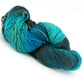 A twisted skein of Great Adirondack Organic DK Cotton yarn by Great Adirondack Yarn Co, Inc. in shades of blue, teal, and green. This hand-dyed yarn boasts a soft and smooth texture, with the variegated colors blending seamlessly for a striking gradient effect.