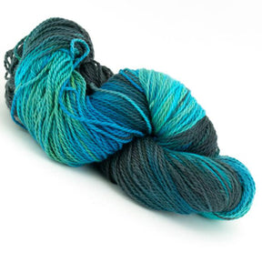 A twisted skein of Great Adirondack Organic DK Cotton yarn by Great Adirondack Yarn Co, Inc. in shades of blue, teal, and green. This hand-dyed yarn boasts a soft and smooth texture, with the variegated colors blending seamlessly for a striking gradient effect.