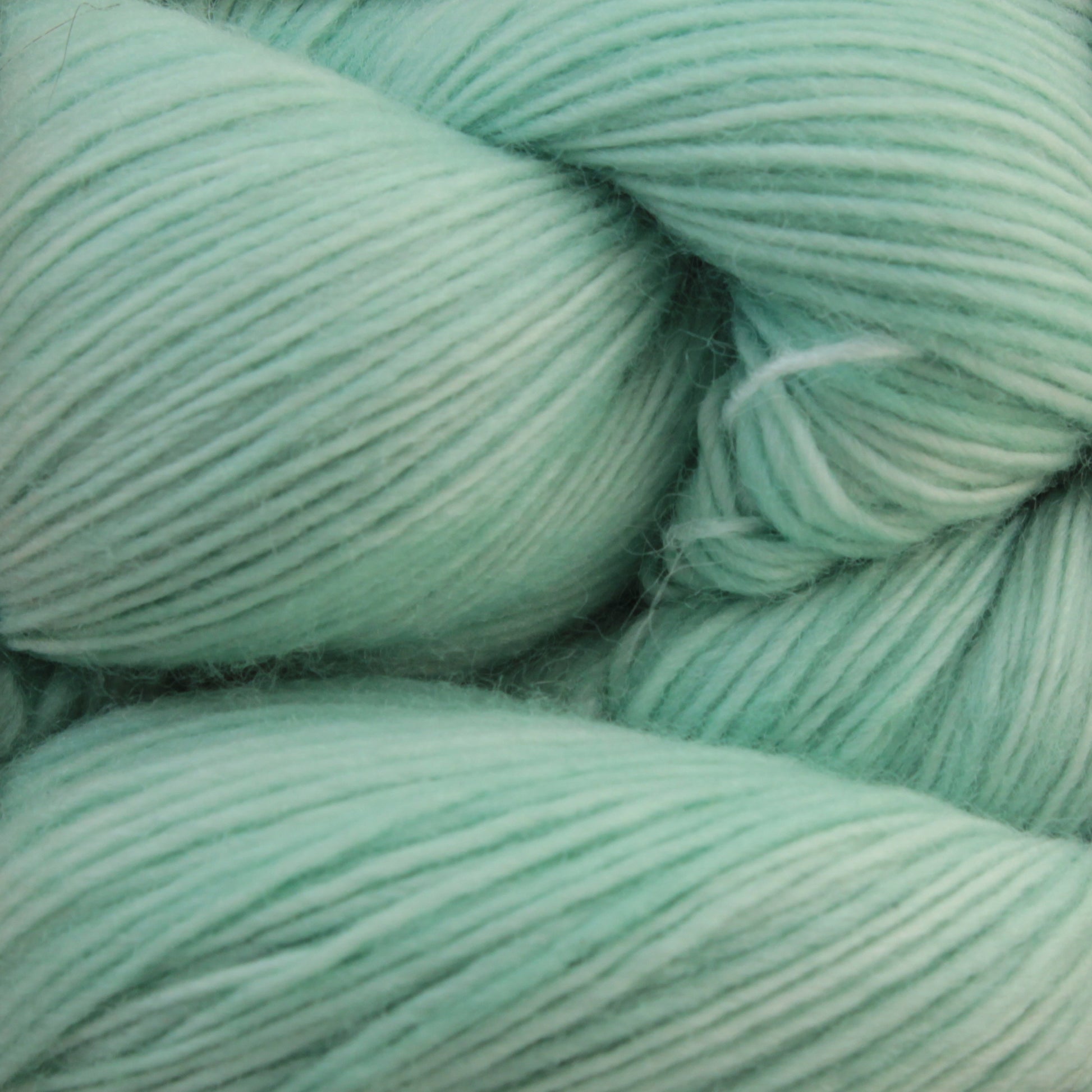 A close-up image of Malabrigo Lace by Malabrigo Yarn in a soft, light mint green hue. The fine, smooth strands are tightly coiled, showcasing the yarn's texture and color. The material appears fluffy and delicate, perfect for knitting or crocheting projects such as knitted shawls.