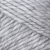 A close-up image of Brown Sheep's Lamb's Pride Worsted Yarn in grey, showcasing its soft and thick strands arranged in a neat, overlapping pattern. The texture appears cozy and slightly fluffy, suitable for knitting or felting projects. The yarn fibers display subtle variations in shade.