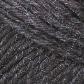 Close-up of Lamb's Pride Worsted Yarn by Brown Sheep, showcasing a thick, dark gray fiber with subtle variations in color. This yarn features interwoven strands of white and lighter gray, giving it a soft and slightly fuzzy texture that makes it ideal for felting projects or Navajo-style weaving.