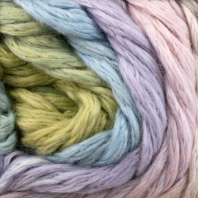 A close-up photo of Cumulus Cotton by Juniper Moon Farm from Knitting Fever / Euro Yarns in pastel shades. The yarn, featuring durable chainette construction, is twisted together, showing a blend of light green, blue, lavender, and pink colors. The texture appears fluffy and cozy, suitable for knitting or crocheting weightless accessories.