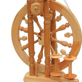 The Kromski Minstrel Spinning Wheel from Kromski North America is a traditional wooden spinning wheel with a large upright wheel, multiple spokes, a spindle, and double treadle foot pedals. Its intricate design features vertical posts and a horizontal frame, expertly built for spinning fibers into yarn.