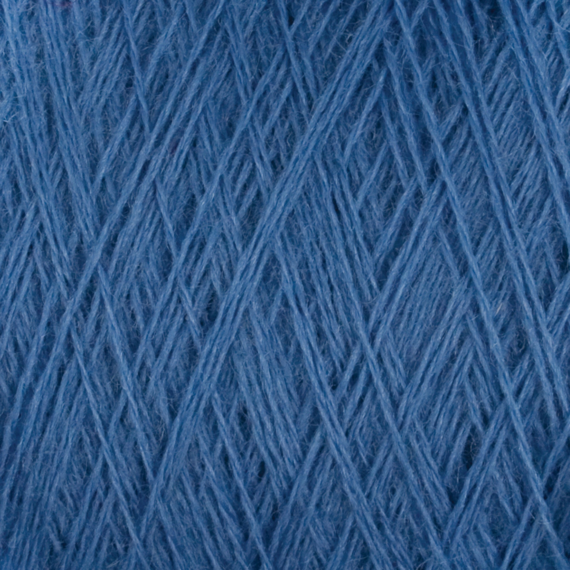 Close-up image of blue, medium grade wool yarn from the Jagger Brothers, Inc.'s JaggerSpun Maine Line 2/20 Yarn on a large cone, displaying a crisscross pattern of fine threads. The texture is soft and fibrous, with intricate layers interweaving. The image emphasizes the detailed structure and color of the JaggerSpun yarns.