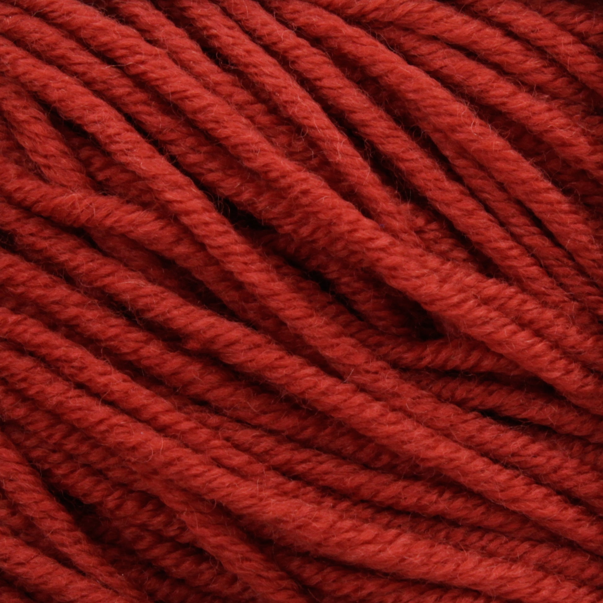 Close-up of a bundle of thick, red Plymouth Select Worsted Merino Superwash from Plymouth Yarn Co., showcasing its rich texture and tightly woven strands. The yarn appears soft and slightly fuzzy, with excellent stitch definition, ready for knitting or crocheting.