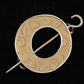 The Single Circle Shawl Pin by Bonnie Bishoff Designs, from the esteemed brand Bonnie Bishoff, boasts a circular shape with an open center and intricate beige and light brown swirling patterns that mimic wood grain. Expertly crafted from polymer clay, this brooch is secured by a straight metal pin that threads through loops on the outer edge of the circle against a black background, making it an elegant closure for knit wearables.