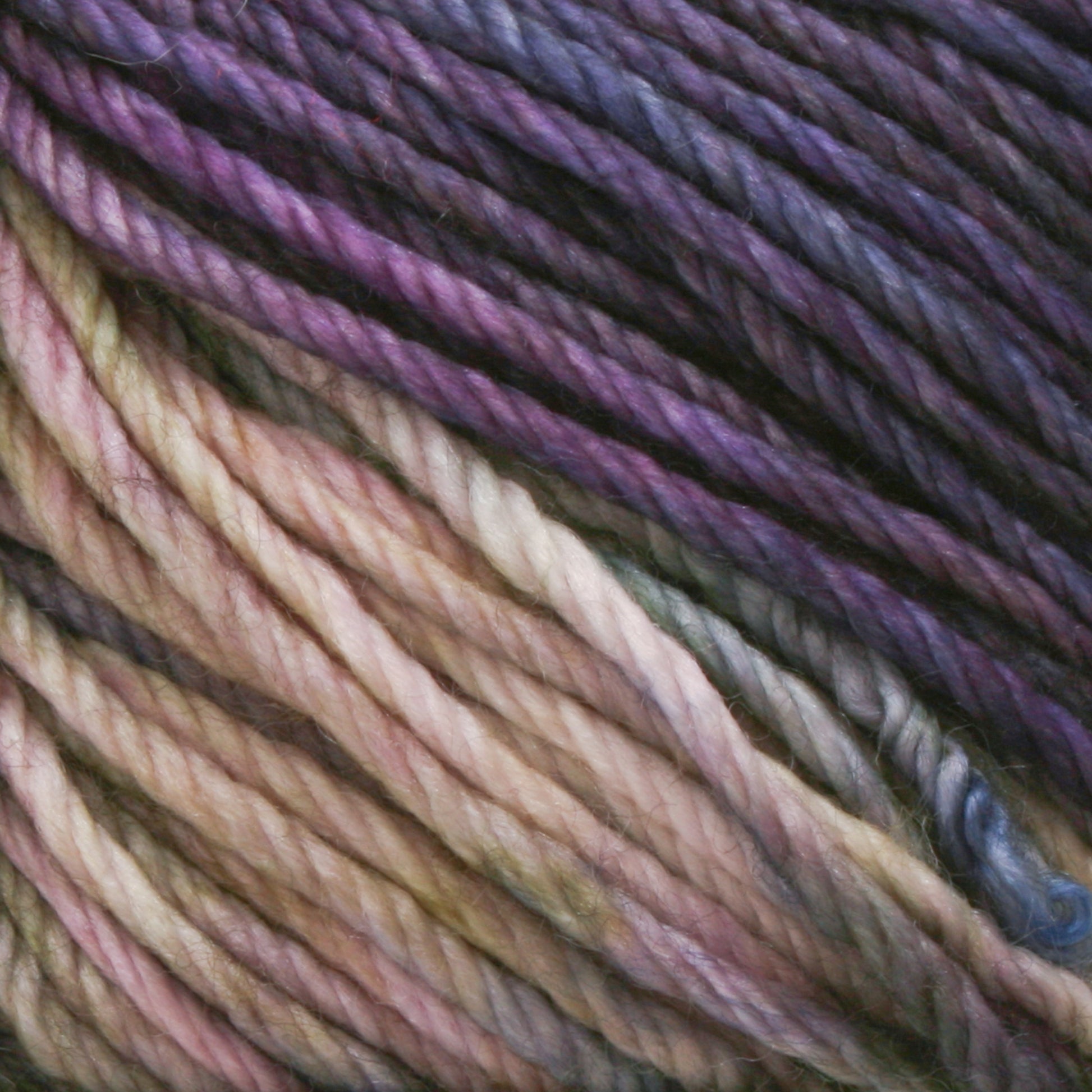 Close-up of multicolored Malabrigo Rios yarn by Malabrigo Yarn, featuring hues of purple, lavender, pink, and cream interwoven in a twisted pattern. The texture appears soft and thick, with the kettle-dyed colors blending smoothly into each other.