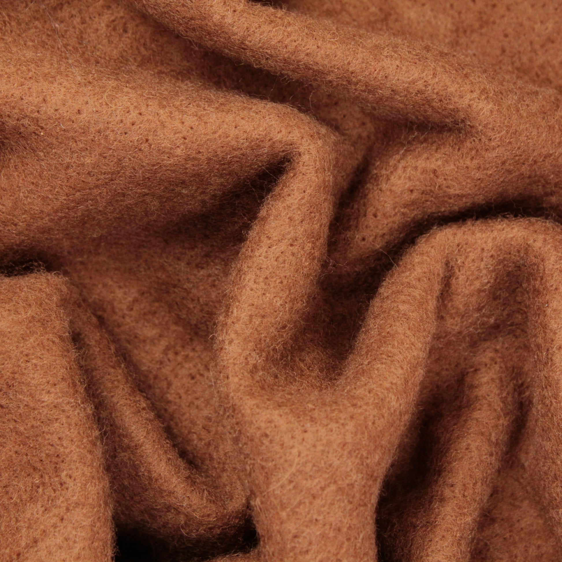 Close-up of Europa Wools Ltd's Merino Prefelt, showcasing its soft, brown wool with visible texture and fibers, highlighted by gentle folds and creases. The material exudes warmth and fuzziness, offering a cozy, inviting appearance—ideal for nuno felting or other felting projects.