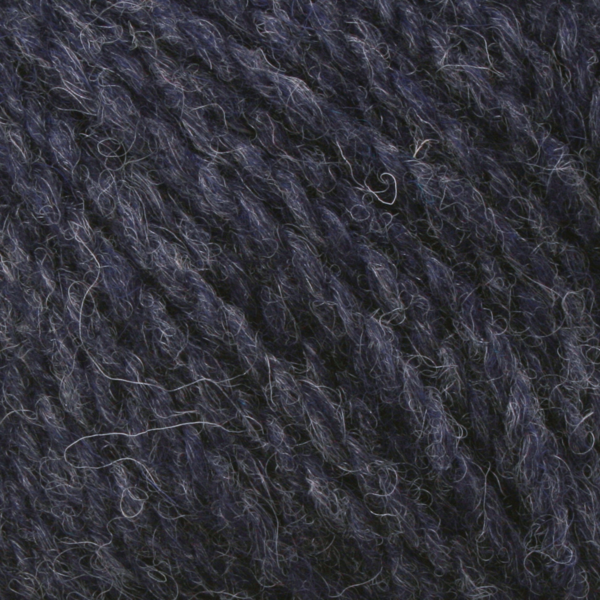 Close-up of the thick, textured Bartlettyarns Maine Wool Yarn in a navy blue worsted weight, with visible fibers and strands. The yarn exhibits a slightly fuzzy appearance, highlighting the soft texture typical of knitting or crocheting materials produced by Bartlettyarns.