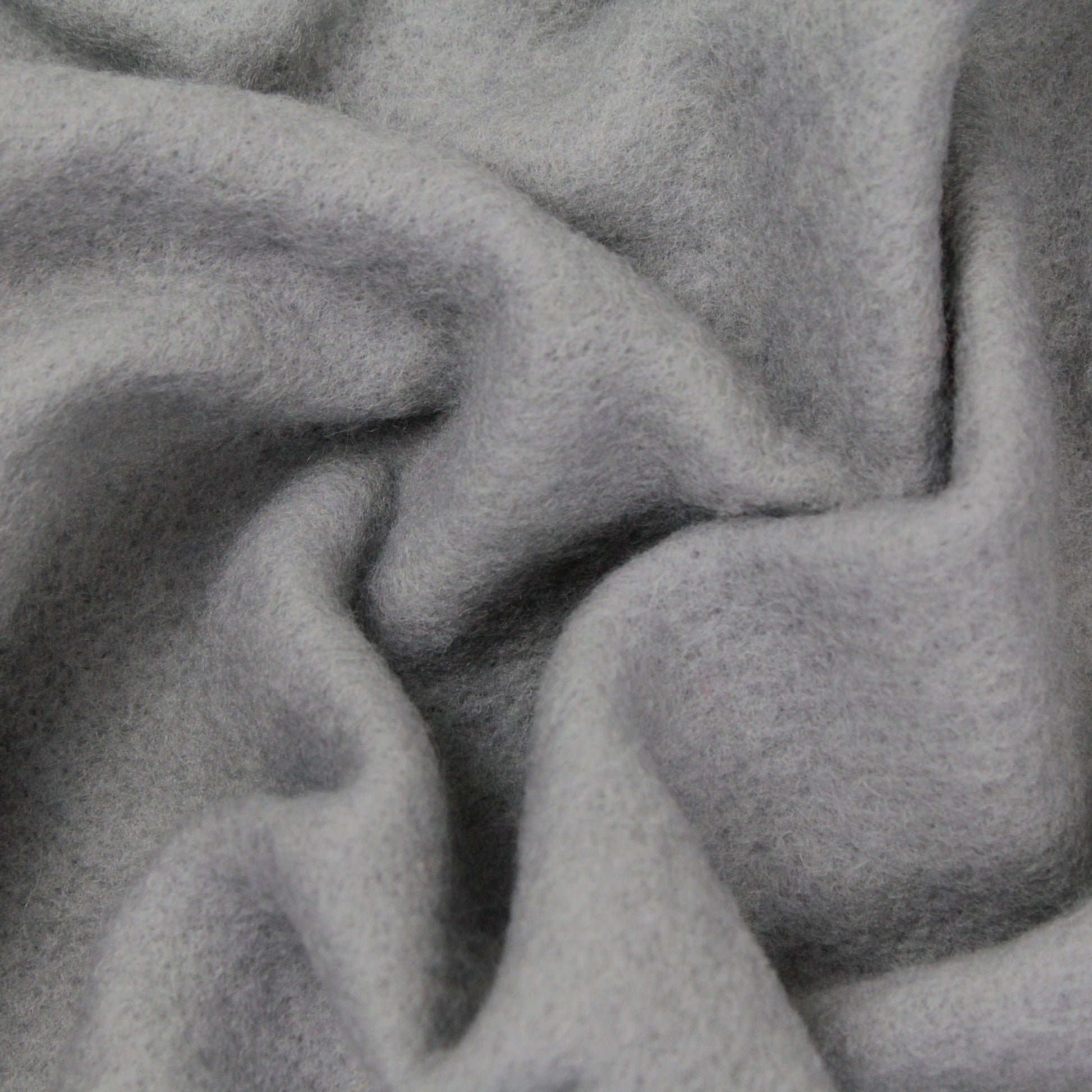 Close-up of soft, light grey Merino Prefelt by Europa Wools Ltd, featuring a textured, felt-like surface. The material is folded and draped in gentle, undulating curves and shadows, making it ideal for felting projects and showcasing its plush and cozy nature.