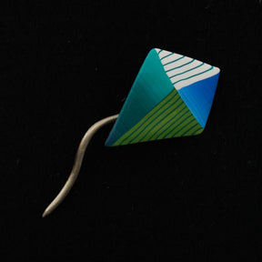 The Short Stick Shawl Pin by Bonnie Bishoff Designs features a colorful, kite-shaped pin with green, blue, and white stripes set against a solid black background. Designed by Bonnie Bishoff, it's perfect for knit wearables or lightweight shawl closures and boasts a curved, tapered metal tail extending from the bottom.