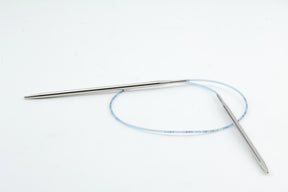 A pair of Skacel Addi Turbo Circular Knitting Needles, connected by a flexible cable, is commonly used for circular knitting. The short circular needles and cable are set against a plain white background, making them perfect for crafting cuffs, collars, or even doll clothes.