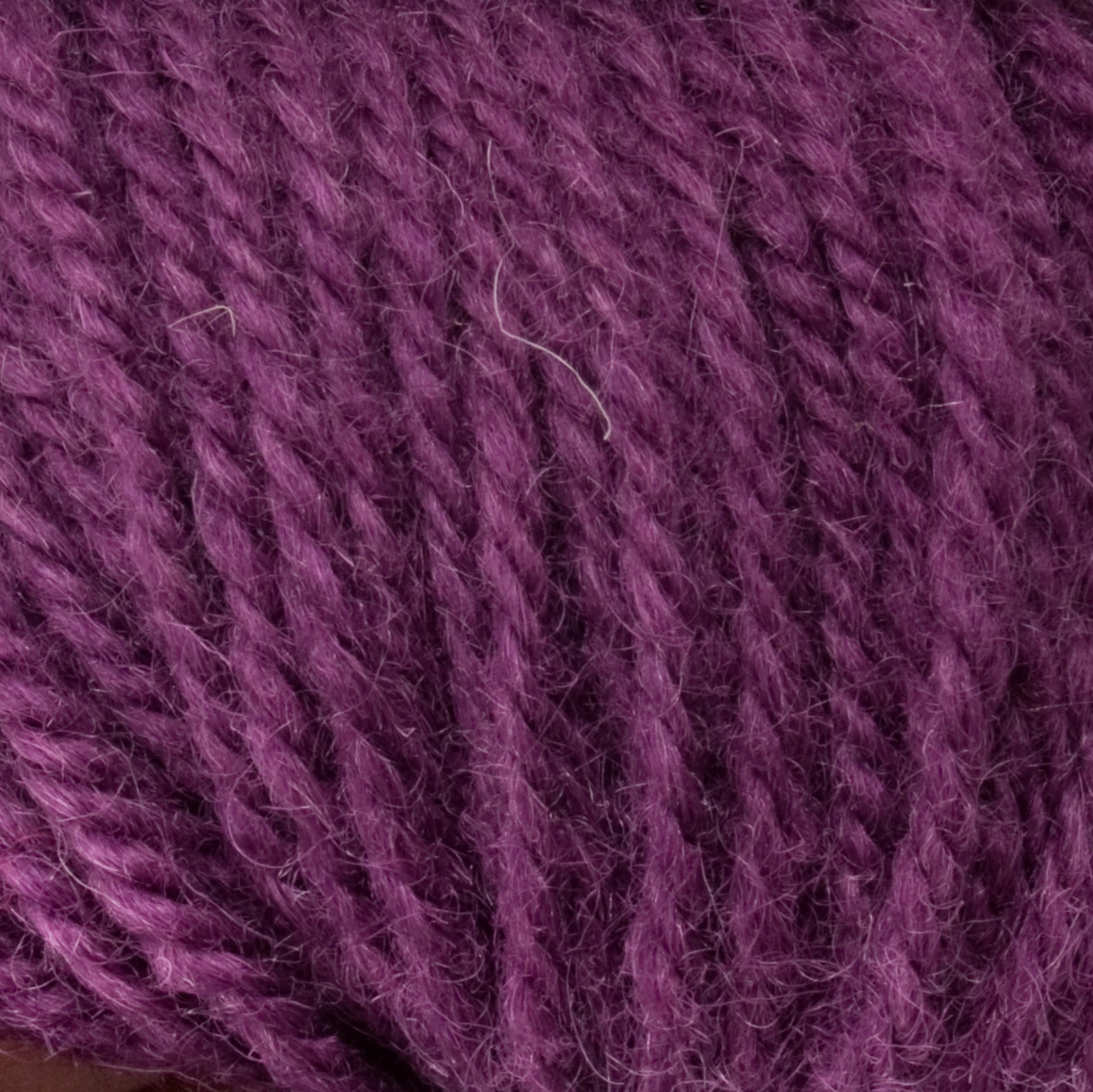 Close-up of Halcyon Deco Rug Wool by Caledonian Dye Works, showcasing its soft, purple yarn with a tightly twisted fiber texture. This image of the 100% wool product highlights the rich, even color and detailed strands of the versatile yarn, emphasizing its plush and cozy appearance.