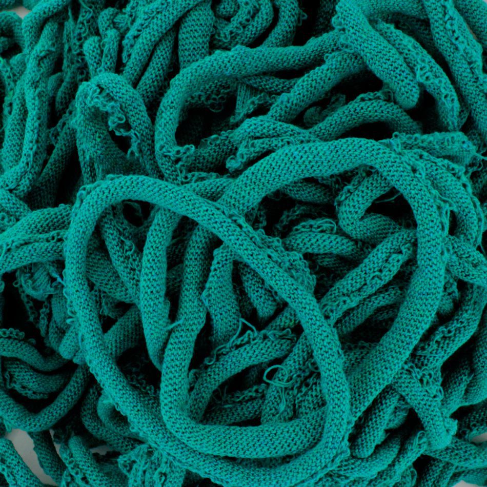 A close-up of a pile of loosely tangled green Harrisville Potholder Loops - Traditional Size Mini Pack by Friendly Loom, made from cotton loops on a traditional loom. The texture of the fabric is clearly visible, appearing soft and slightly stretchy. The loops intertwine in various directions, creating an intricate pattern.