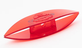 A close-up image of the Handy Hands Tatsy Tatting Shuttle, 4", a red plastic object shaped like an elongated oval with a flat base. The center features a small, rectangular raised section with a hole. An engraved planet with a ring logo is visible on the outer surface.