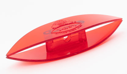 A close-up image of the Handy Hands Tatsy Tatting Shuttle, 4", a red plastic object shaped like an elongated oval with a flat base. The center features a small, rectangular raised section with a hole. An engraved planet with a ring logo is visible on the outer surface.