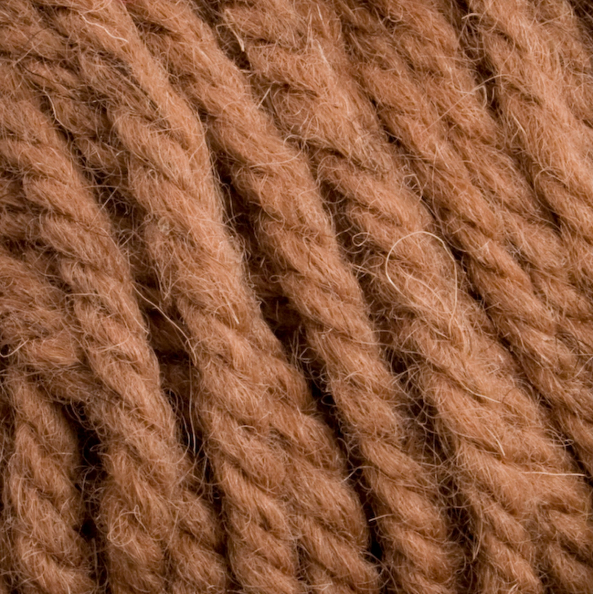 Close-up view of thick, brown strands from the Halcyon Yarn Classic Rug Wool by Caledonian Dye Works intertwined tightly, creating a textured, fibrous pattern reminiscent of sturdy rope. The image highlights the individual fibers and the coarse surface, akin to what rug weavers might appreciate for its robust design.