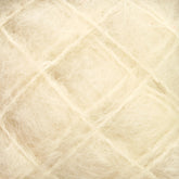 Close-up image of Victorian Brushed Mohair Yarn from Caledonian Dye Works shows a beige, fibrous, and textured material with a grid-like pattern. The surface appears soft and tangled with intersecting lines forming a crisscross design, reminiscent of luxurious mohair. The overall effect is a mix of organic and geometric elements.