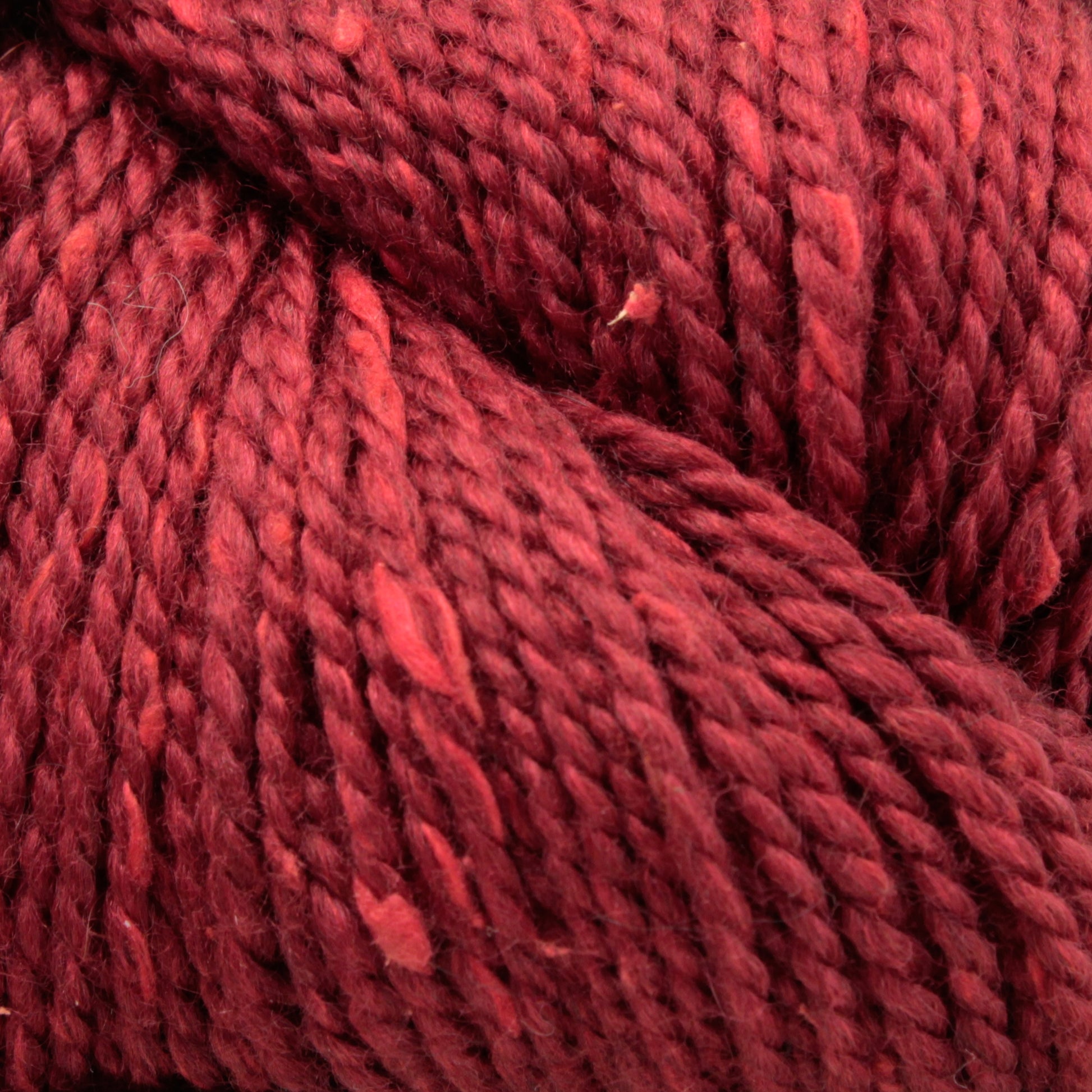 Close-up shot of Acadia by The Fiber Company in deep red, showcasing its thick, twisted texture and fibers. The yarn from The Fibre Co. (UK) Ltd appears soft and plush with subtle variations in color and small specks of lighter red throughout, creating a subtle tweed effect reminiscent of natural scenic beauty.