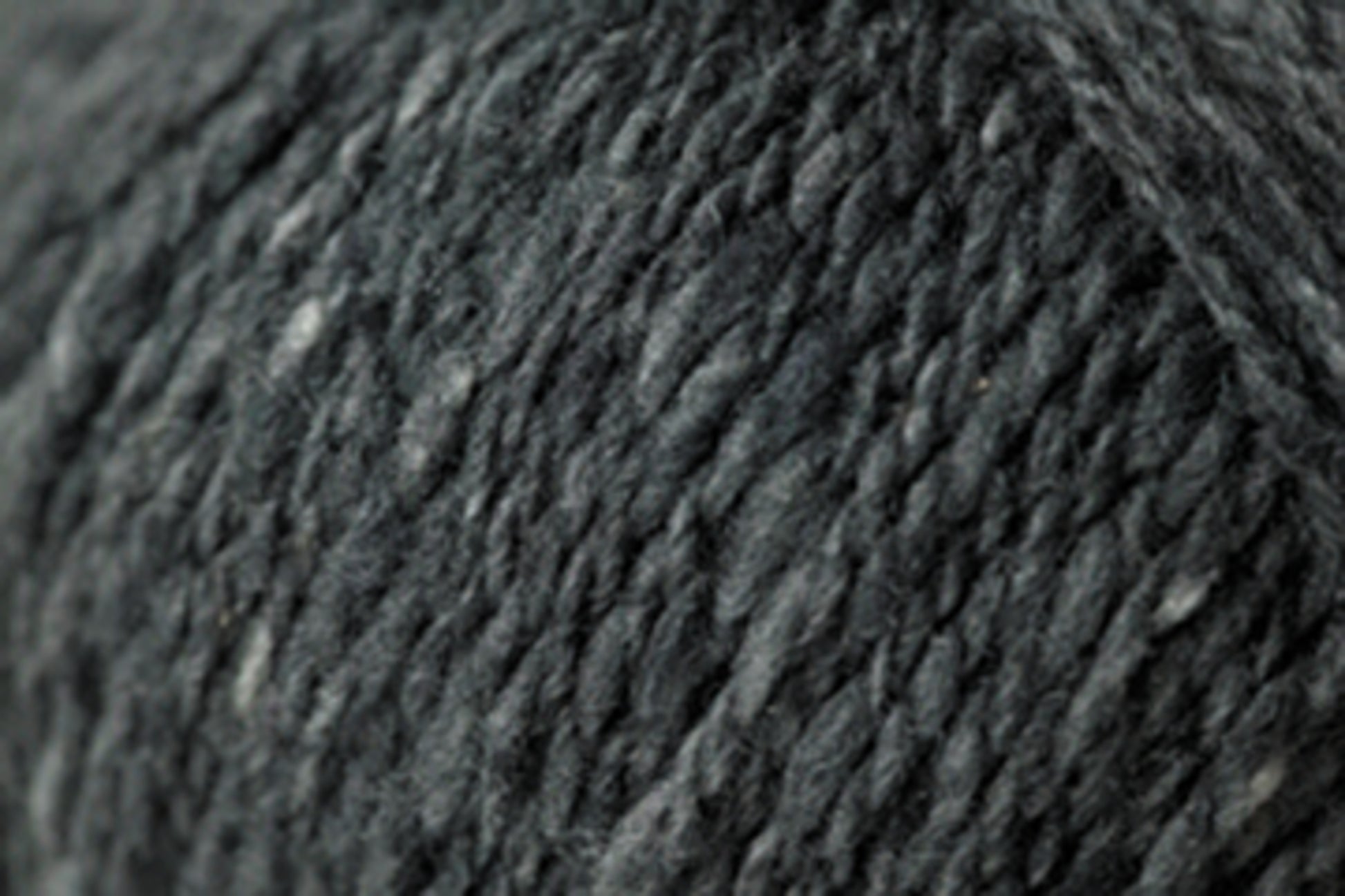 Close-up image of dark gray Jo Sharp Silkroad DK Tweed yarn from Kingfisher Yarn & Fibre, showcasing its soft and slightly fuzzy surface. The yarn appears dense and tightly spun, with subtle variations in shade that add depth to the monochromatic color.