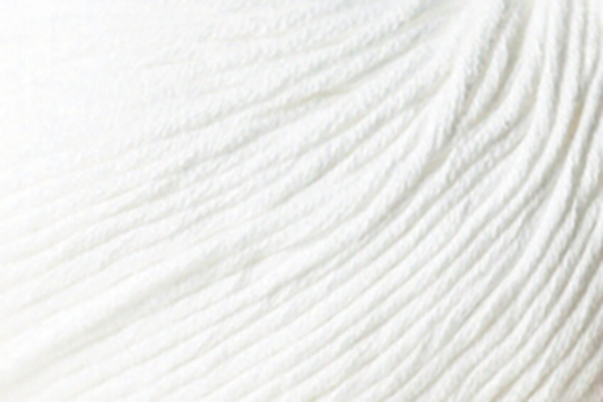 A close-up of white, textured fabric made from Jo Sharp Soho Summer DK Cotton yarn by Kingfisher Yarn & Fibre, featuring soft ridges and folds that create subtle, wave-like patterns. The material appears smooth and slightly reflective.