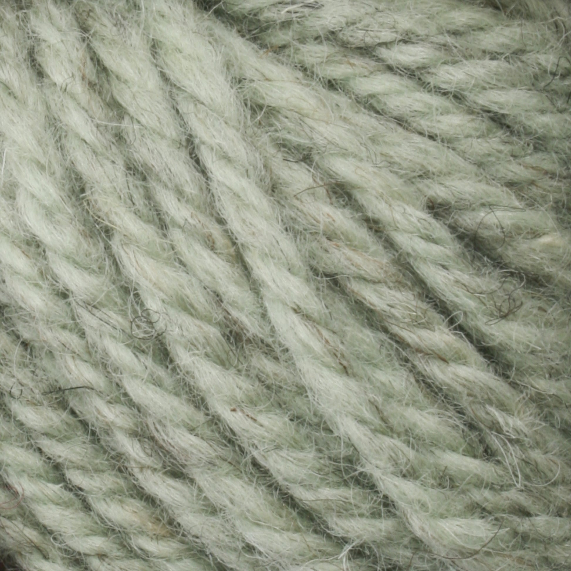 A close-up view of a spool of Halcyon Yarn Classic Rug Wool in light green from Caledonian Dye Works. The thick, twisted fibers boast a soft and fuzzy texture. This high-quality yarn showcases tightly wound strands with a detailed weave pattern, making it perfect for rug weavers using Classic Rug Wool techniques.