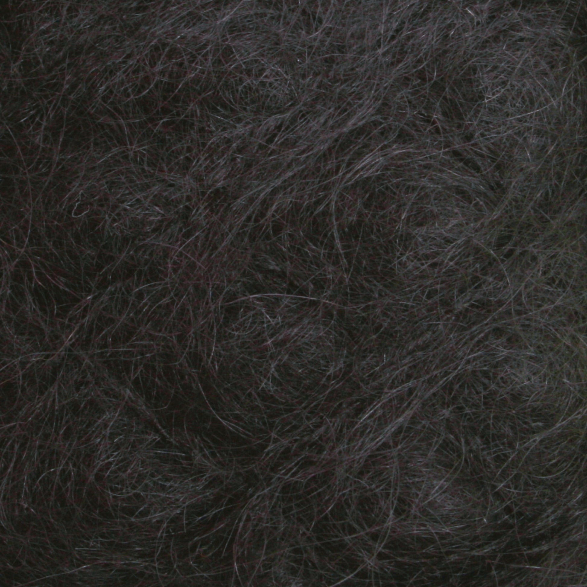 Here's a close-up view of the Victorian Brushed Mohair Yarn | Large Skein by Caledonian Dye Works. It features a dense, textured mass of dark and slightly wavy fibers. The colors range from dark gray to nearly black, with some lighter gray strands intermingled. This luxurious mohair appears tangled and intertwined, creating a chaotic, organic pattern reminiscent of Victorian yarns.