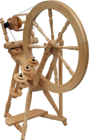 The Kromski Interlude Spinning Wheel from Kromski North America showcases a large wheel on the right connected to a smaller wheel and multiple spindles on the left. Crafted from European alder and birch, this apparatus exudes a traditional, handcrafted appeal with intricate detailing on its legs and supports.