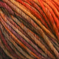 Close-up of a ball of multicolored Malabrigo Rios yarn in warm hues, including orange, red, yellow, and brown, with thick, twisted strands creating a textured pattern that showcases its kettle-dyed colors.