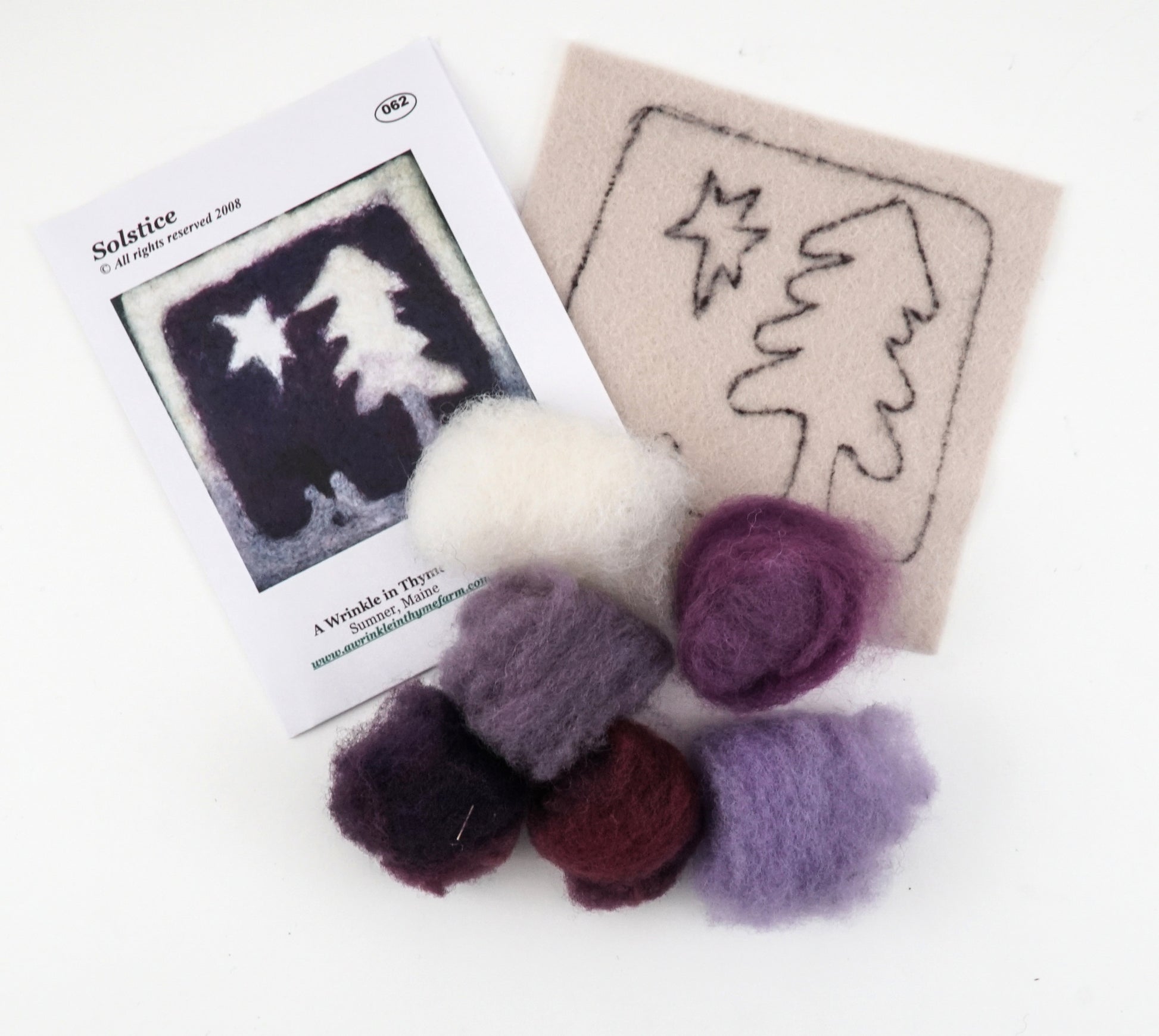 The "Thyme Tile Felting Kit (no tools)" by A Wrinkle in Thyme Farm includes a printed design featuring a tree and star silhouette, a beige felt piece with the design's outline, and several small balls of wool roving in shades of purple, red, and white. Ideal for beginner felters!