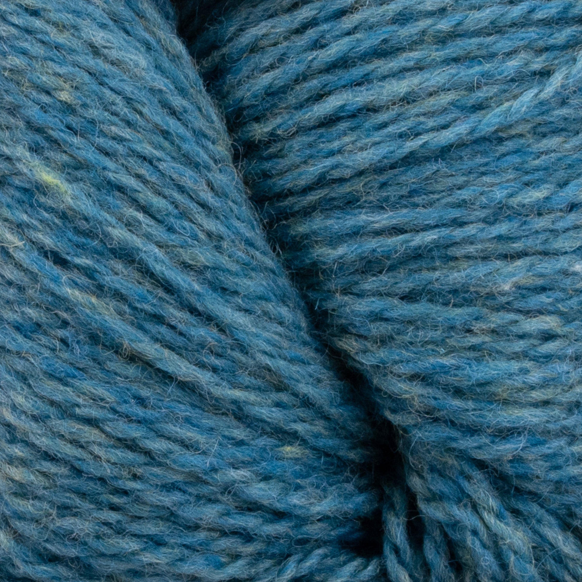 Close-up view of a blue yarn skein interwoven with shades of green and grey. The texture is soft and slightly fuzzy, indicative of the Patagonia Organic Merino by Juniper Moon Farm. The image showcases the intricate details of the GOTS certified fibers, highlighting the yarn's thickness and twist from Knitting Fever / Euro Yarns.