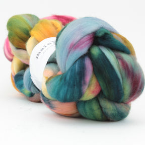 A skein of Nube by Malabrigo, featuring a blend of hand-dyed hues in blue, green, pink, yellow, and orange. The soft, thick strands of Merino wool by Malabrigo Yarn are twisted together with a partially visible white label against a plain, light background.