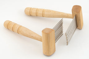 Two Acorn Petite Combs from Sunrise Metal Works, featuring wooden handles and multiple parallel metal prongs that resemble petite single row combs, are aligned in the same direction akin to a carding medium for coarser wools. The tools are positioned at an angle, with one handle resting on the other against a plain white background.