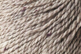 A close-up image of Jo Sharp Silkroad DK Tweed by Kingfisher Yarn & Fibre in beige, showcasing subtle hints of purple fibers intertwined. The texture appears soft and twisted, revealing the detailed fibers and strands. This thick, textured DK weight yarn seems perfect for knitting or crocheting luxurious projects.