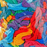 An assortment of colorful Harrisville Potholder Loops - Traditional Size Mini Pack from Friendly Loom, featuring vibrant hues like blue, red, green, yellow, purple, and orange, are gathered together in a chaotic but visually pleasing arrangement. The texture of the woven fabric is clearly visible.