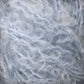 Close-up image of a light blue textured yarn from Caledonian Dye Works' Victorian Bouclé Mohair Yarn. The fibers are wispy, fluffy, and curly, creating a soft and fuzzy appearance. The strands are intertwined in a complex and dense pattern, akin to the Victorian era's intricate details, showcasing the yarn's texture.