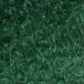 Close-up image of green fuzzy textured fabric with tightly coiled curls, resembling green curly hair or textured fibers intricately interwoven. The fabric, crafted using Caledonian Dye Works' Victorian Bouclé Mohair Yarn, appears soft and plush with a rich emerald hue and various greens.