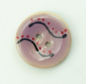 The Coco Enamel Fa la la Button by Buttons Etc. is a round, two-hole accessory, boasting a creamy beige edge and a light pink center. It features a decorative design with curved black lines and small red dots. Measuring 1 1/8 inches in diameter, this glossy button appears to be made of plastic.