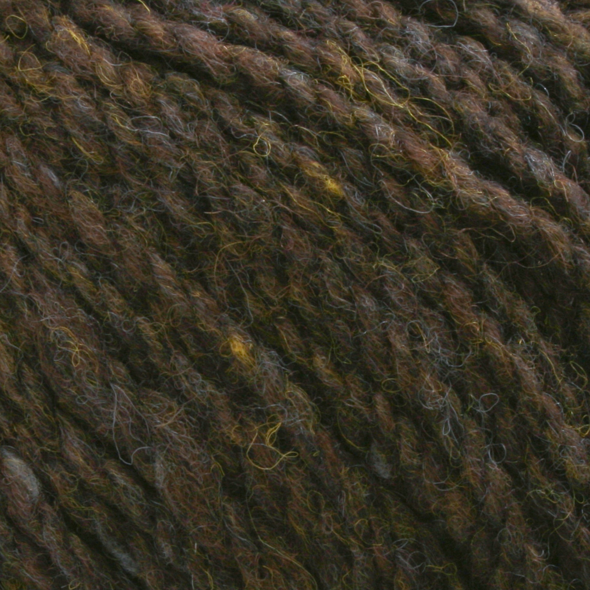 Close-up image of Harrisville Designs' Harrisville Shetland Yarn - Unwashed Cones, showcasing a blend of dark brown, gray, and green fibers. The texture appears soft and slightly fuzzy, with threads twisted together to form a thick and cozy strand, ideal for lightweight blankets or Fair Isle knitting designs.