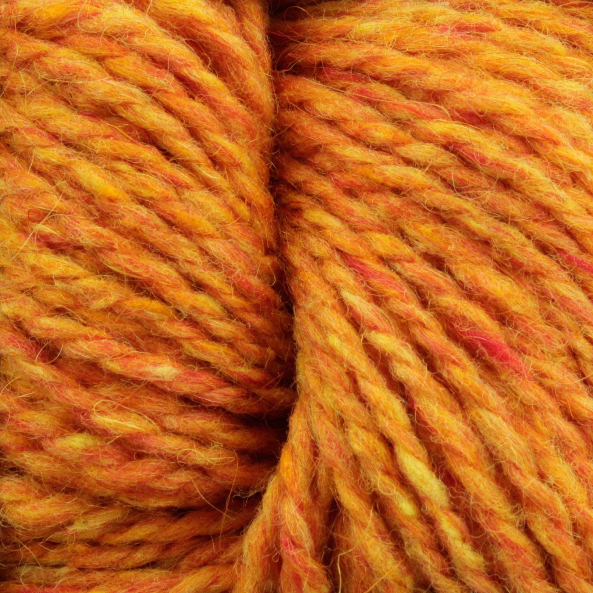 Close-up of Harrisville Designs' Peace Fleece Yarn in orange with subtle hints of yellow and red. The thick, textured fibers are twisted together into a wool and mohair blend, creating a rich, warm tone that resembles the colors of autumn leaves—ideal for worsted weight knitting projects.