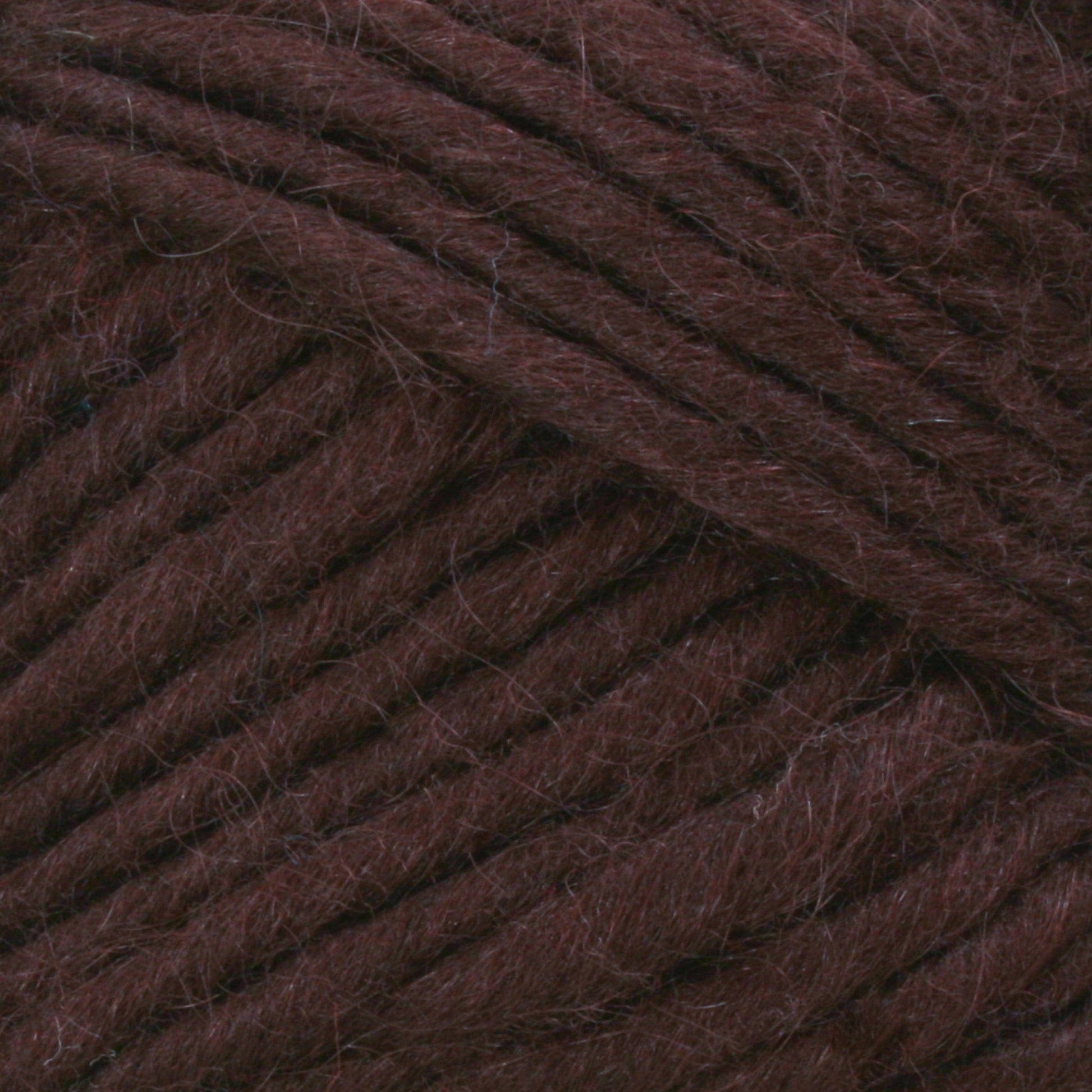 Close-up image of Lamb's Pride Bulky Yarn by Brown Sheep, showcasing the texture and strands tightly wound together in a dark brown hue. The fibers appear soft and slightly fuzzy, with a rich, deep color. Perfect for knitters and crocheters, the image highlights the intricate details and uniformity of the yarn's thickness.