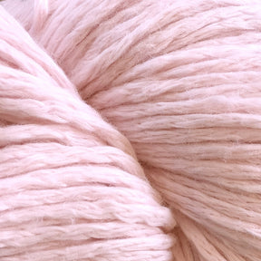 A close-up image of Cumulus Cotton by Juniper Moon Farm from Knitting Fever / Euro Yarns reveals the individual fibers and twists, showcasing its fluffy and cozy texture attributed to its durable chainette construction. The soft, pink yarn radiates a calm and gentle feeling through its warm pastel color.