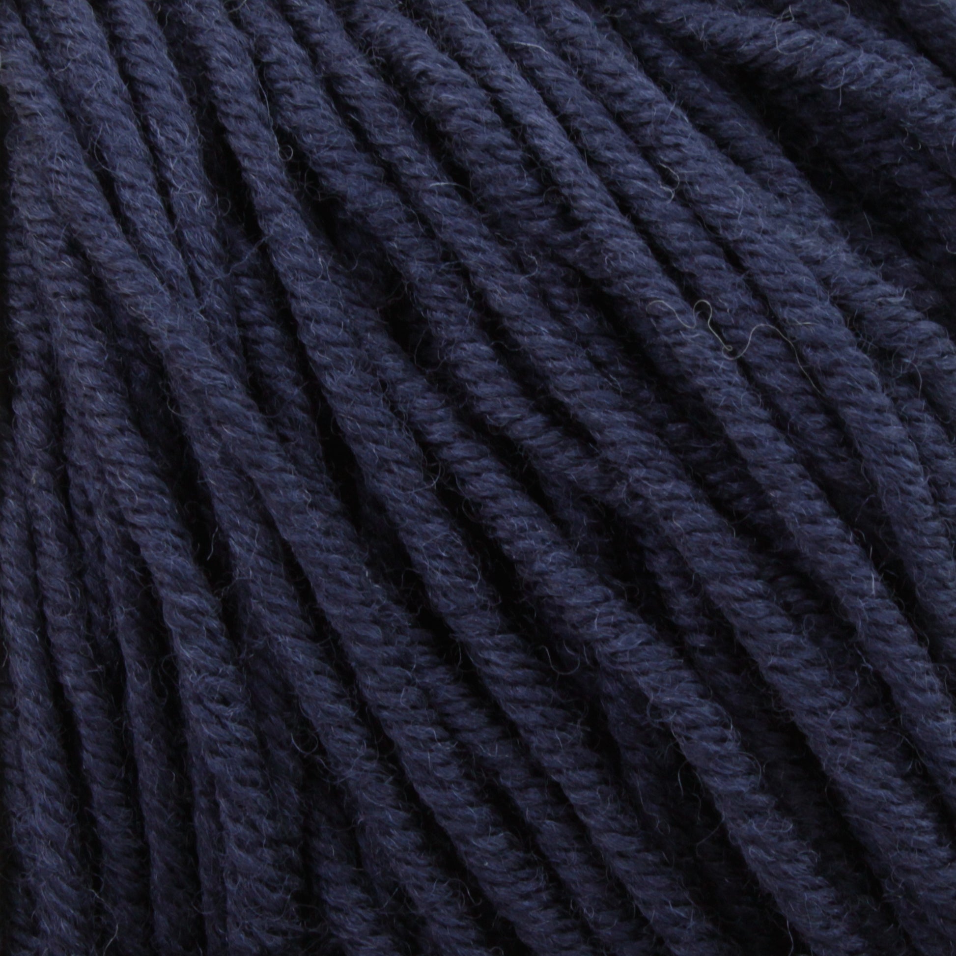 A close-up view of Plymouth Yarn Co.'s Plymouth Select Worsted Merino Superwash in dark blue, highlighting the texture and twists of the fibers. The yarn appears thick and tightly wound, creating a rich, deep hue with superior stitch definition.