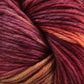 A close-up image of Malabrigo Yarn's Malabrigo Arroyo reveals tightly coiled strands of sport weight superwash merino wool. The yarn showcases a rich blend of colors, including deep burgundy, purple, and shades of orange, offering a warm and textured appearance perfect for lightweight garments. The fibers look soft and thick.