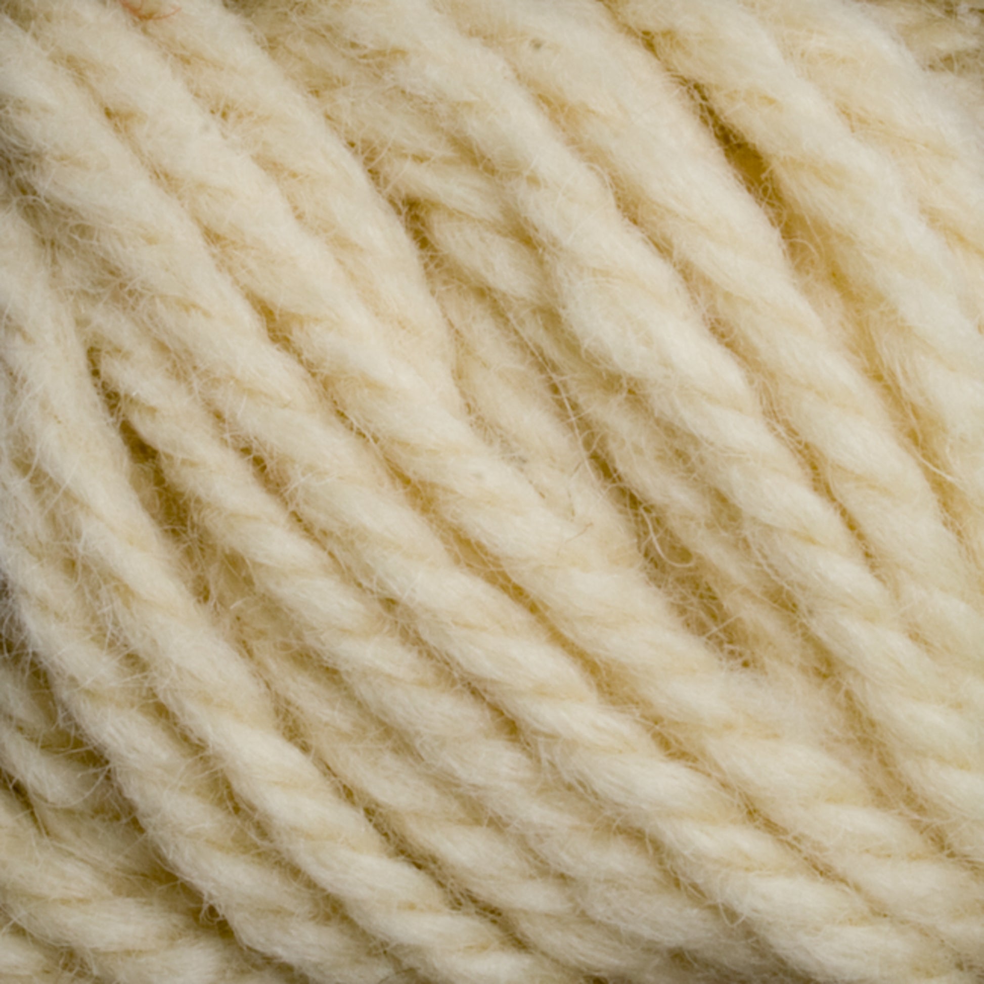 Close-up of thick, twisted strands of Halcyon Yarn Classic Rug Wool in light cream from Caledonian Dye Works, showcasing its soft texture and fibrous details. The wool appears fluffy and ready for knitting or crocheting projects. This yarn offers a neutral, natural look that's perfect for rug weavers or those seeking hand-dye adventures.