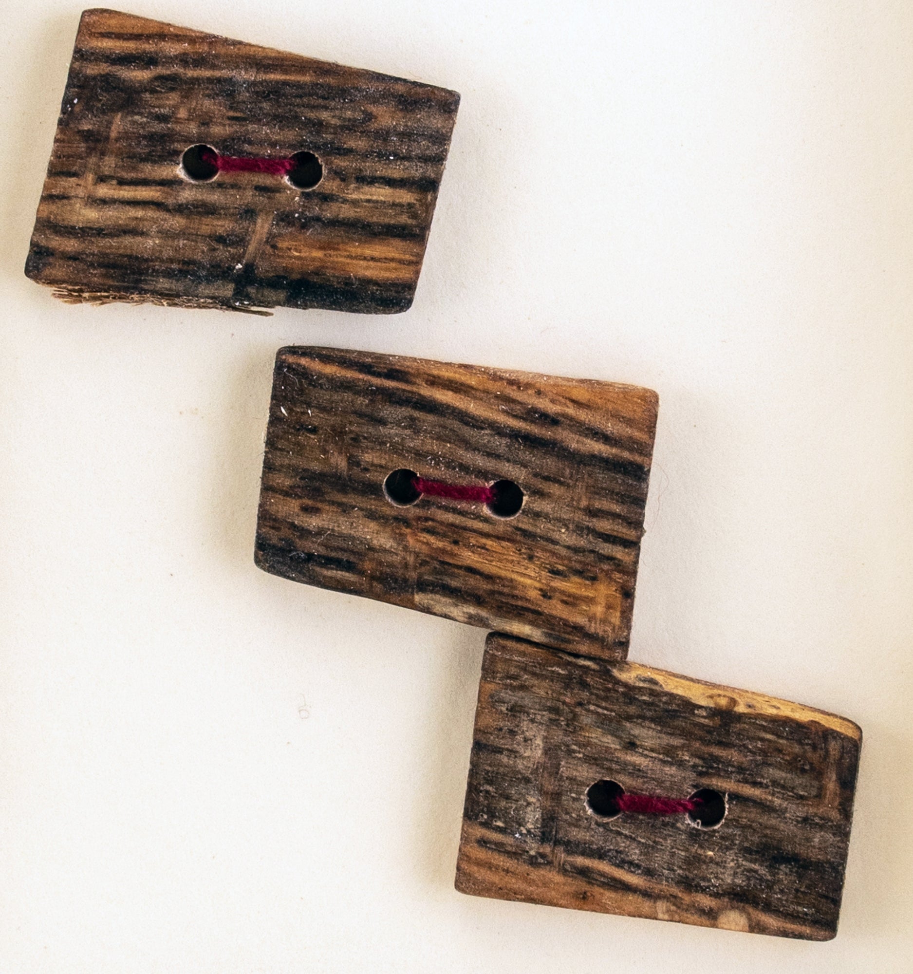 Three square buttons from the "Round or Square Buttons - Mixed Woods" collection by Favour Valley Woodworking, each handmade with visible wood grain patterns and featuring two holes, are strung with red thread and arranged in a diagonal line against a light background.